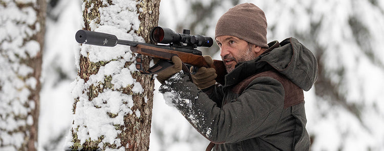 Jäger mit Gewehr und Carinthia Jagdbekleidung im Winterwald